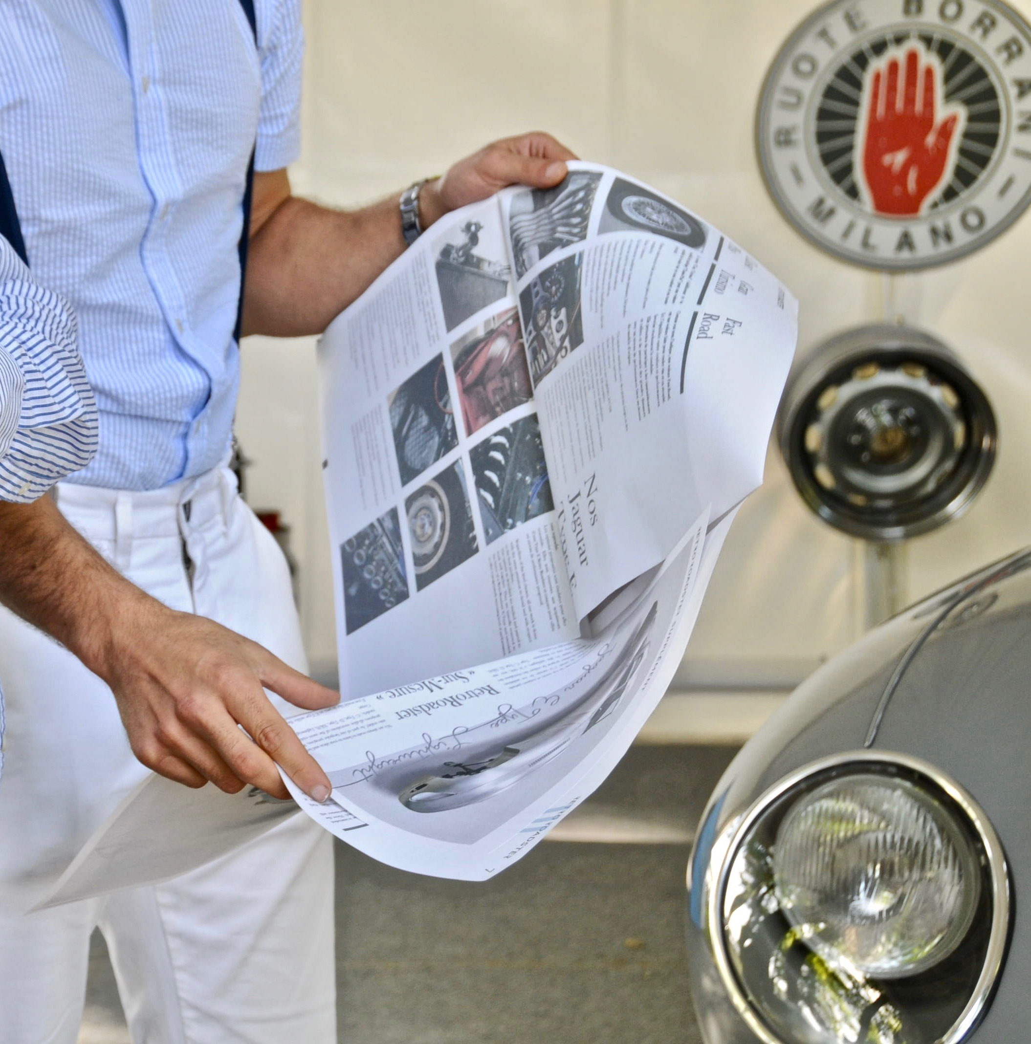 A reader holding the RetroRoadster newspaper beside a classic car in a workshop